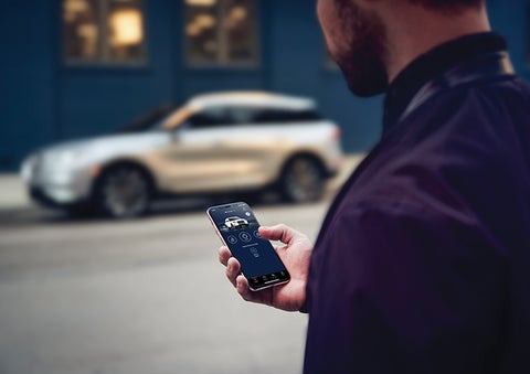 A person is shown interacting with a smartphone to connect to a Lincoln vehicle across the street. | Irwin Lincoln Laconia in Laconia NH