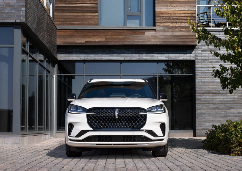 A white 2025 Lincoln Aviator® SUV is shown parked outside a modern building with gray brick and wood accents. | Irwin Lincoln Laconia in Laconia NH