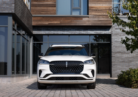 A white 2025 Lincoln Aviator® SUV is shown parked outside a modern building with gray brick and wood accents. | Irwin Lincoln Laconia in Laconia NH