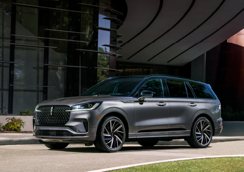 A gray 2025 Lincoln Aviator® SUV is parked outside a modern building showcasing the driver’s side of the vehicle. | Irwin Lincoln Laconia in Laconia NH
