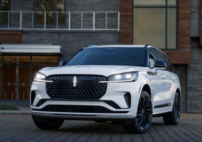 A white 2025 Lincoln Aviator® SUV is shown parked outside a modern building with gray brick and wood accents. | Irwin Lincoln Laconia in Laconia NH