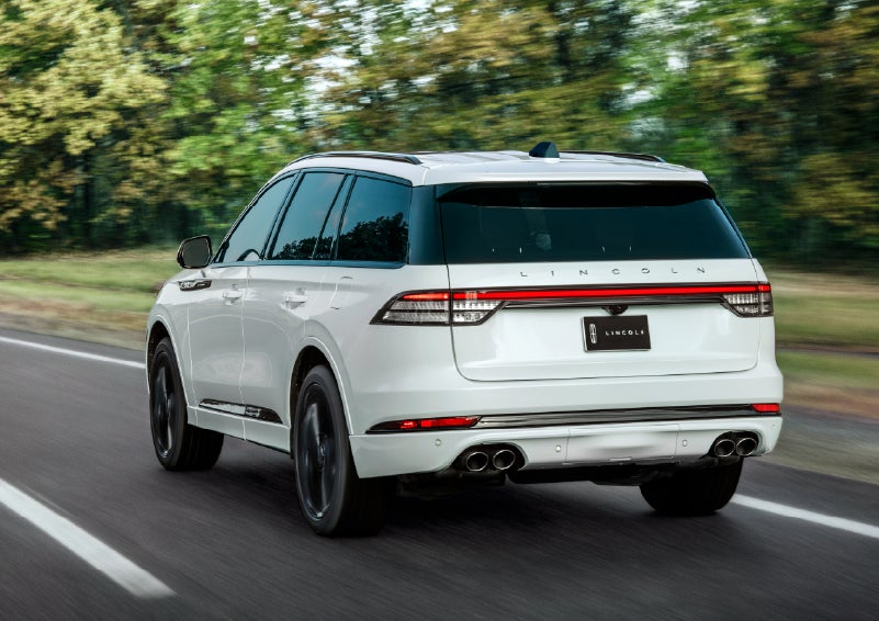 A white 2026 Lincoln Aviator® SUV is being driven away down a road lined with colorful trees. | Irwin Lincoln Laconia in Laconia NH