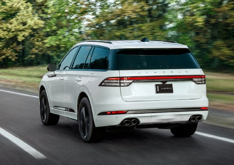 A white 2026 Lincoln Aviator® SUV is being driven away down a road lined with colorful trees. | Irwin Lincoln Laconia in Laconia NH