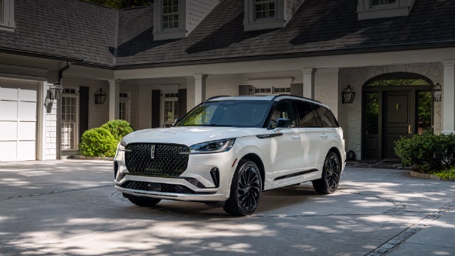 A white 2026 Lincoln Aviator® SUV is parked in the driveway of a luxury home. | Irwin Lincoln Laconia in Laconia NH
