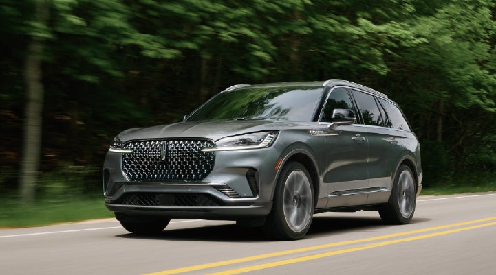 A 2027 Lincoln Aviator® SUV is being driven down a road lined with trees. | Irwin Lincoln Laconia in Laconia NH
